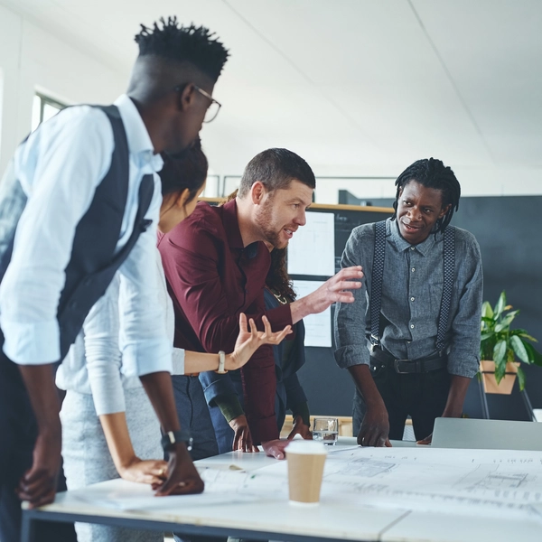 People collaborating around a desk with large plans laid out