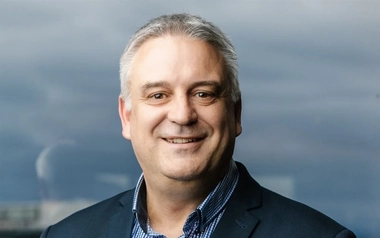 Professional headshot of Andrew Reynolds wearing a dark blazer and patterned shirt.