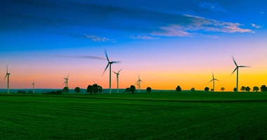 wind turbines on green field and against blue and orange sky