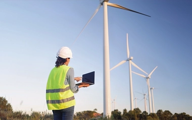 Person using a laptop beside wind turbines in a wind farm