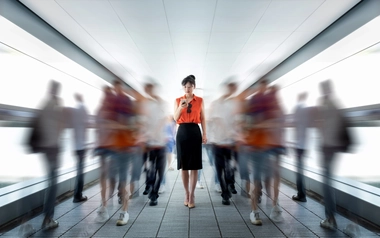 Person looking at a mobile phone in a corridor with blurred people walking by.