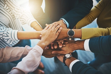 Group of people standing with hands stacked together, symbolizing unity and teamwork