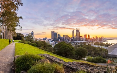 Sunrise view of Perth’s city skyline from a park with trees and a walking path.
