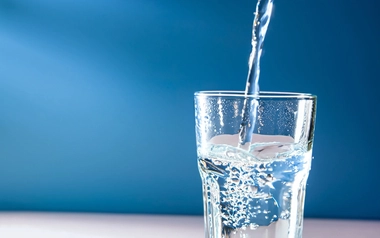 AdobeStock_634925048.jpeg-Water pouring into a clear glass cup against a plain blue background