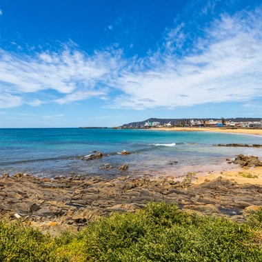 Rocky shoreline and sandy beach beside blue ocean at Burnie waterfront.