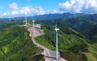 Wind turbines on green hills with winding access roads viewed from above.