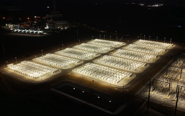 Aerial view of a lit battery storage facility at night with rows of containers and power lines
