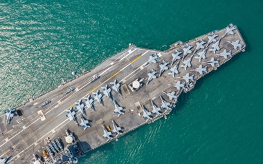 Aerial view of Navy ship carrying jets surrounded by crystal green ocean