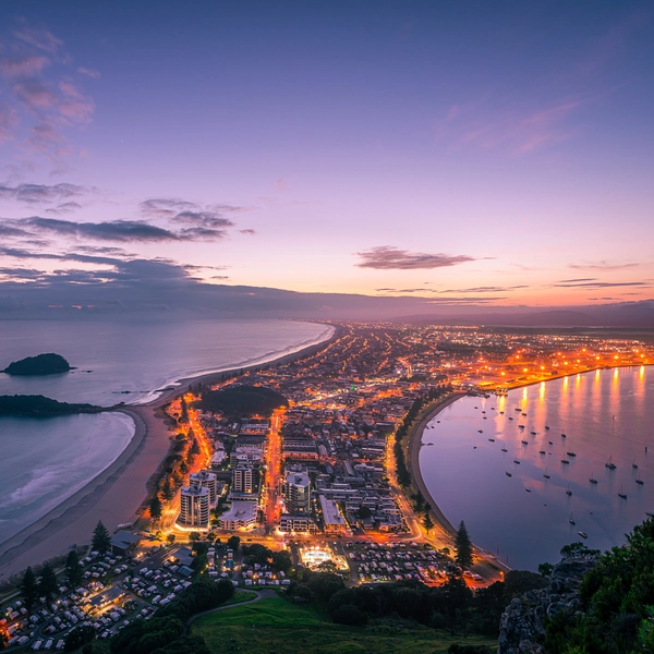 Aerial view of a coastal city at sunset with lights along the shoreline