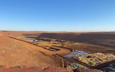 Open pit mine with surface water pools and drainage channels in a dry landscape.