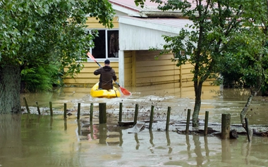 David Norman in a canoe moves through floodwater around a house