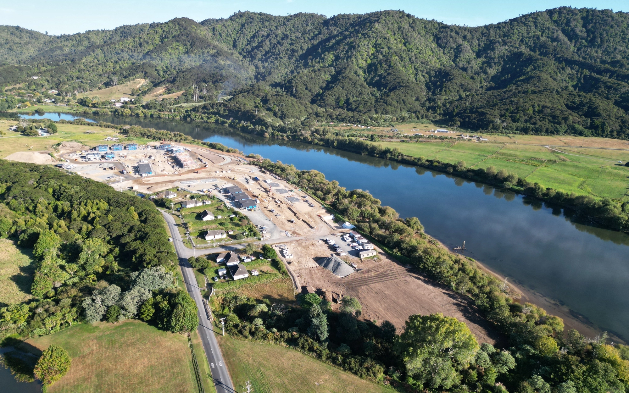 Construction site beside river with forested hills in background