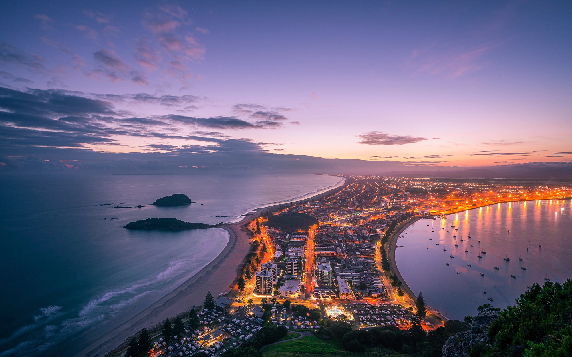 Aerial view of coastal city with curved shoreline and lights at dusk
