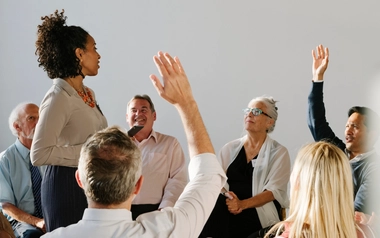 Group seated in a circle with several people raising their hands during a discussion