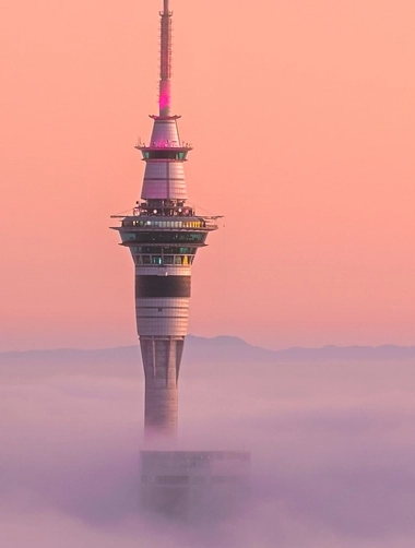 City tower rising above thick fog with orange sunset sky