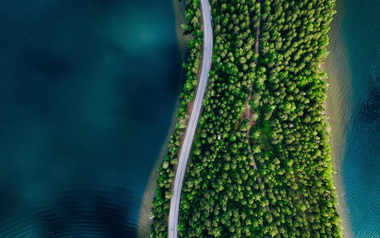 narrow strip of land with trees and a road, surrounded by blue water