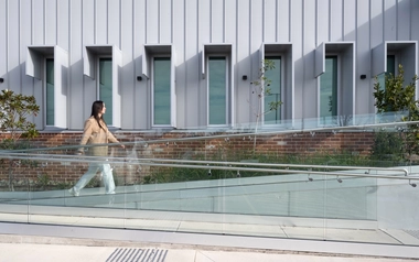 Person walking on a glass-railed ramp beside a modern building.