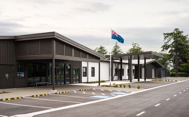 Front entrance of the Burnham Health and Wellness Centre with covered walkway, New Zealand flag, and marked parking bays.