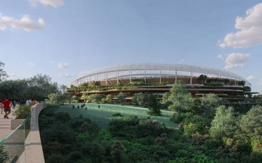 People walk toward a circular stadium with green terraces surrounded by trees