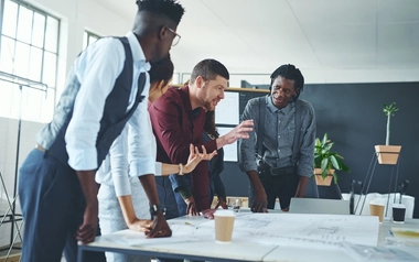 People collaborating around a desk with large plans laid out