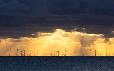 Offshore wind turbines across the ocean under dark clouds with sunlight