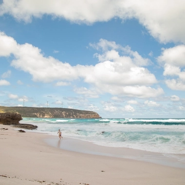 Boy running from waves on the beach with wind turbines on cliff in the background