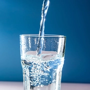 AdobeStock_634925048.jpeg-Water pouring into a clear glass cup against a plain blue background