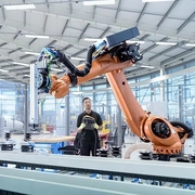 Industrial robotic arm operating in a modern factory, with a technician standing nearby holding a control device