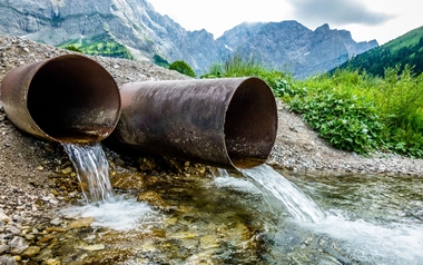two large metal pipes discharging water into a rocky stream