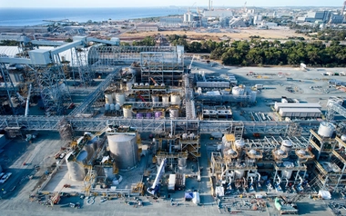Aerial view of an industrial facility with tanks and pipework beside the coast.