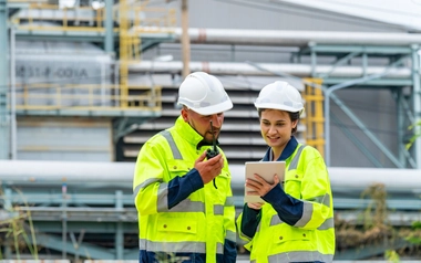 Two workers in high-visibility jackets and helmets standing in front of industrial equipment