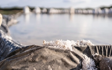 Salt crystals on a lined evaporation pond, with water and salt formations in the background.