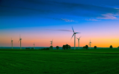 wind turbines on green field and against blue and orange sky