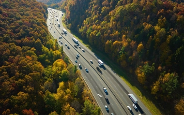 Aerial view of a busy highway cutting through a forest with vibrant autumn foliage