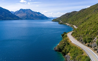 Winding road beside a blue lake with mountains in the background