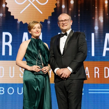 Two people on an awards stage with Rebecca Want holding a trophy.
