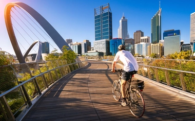 Cyclist riding on a boardwalk near the Elizabeth Quay bridge with Perth's skyline in the background.