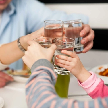 Several hands holding up glasses of water at a dining table