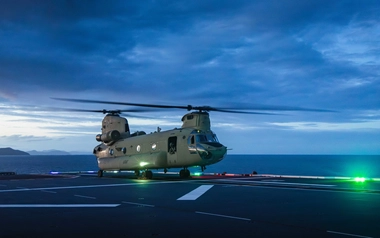 Twin-rotor helicopter on a ship landing deck at dusk over the ocean.