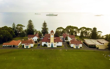 Aerial view of waterfront buildings and open grounds beside the sea with ships offshore.