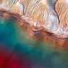 Aerial view of a tailings pond with red and blue water near a shoreline.