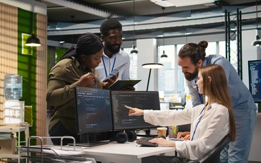 Team gathered around a desk while looking computer screens