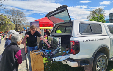 Person showing equipment from open vehicle at outdoor event