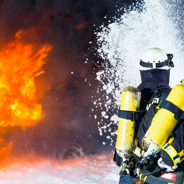 Firefighters in protective gear spray foam toward a large fire