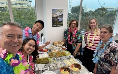 People wearing leis gathered around a table with food in office