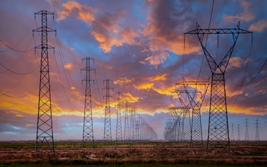 High-voltage power transmission towers stretching across a landscape at sunset with dramatic clouds